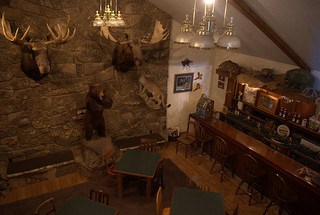 A stone fireplace with mounted hunting trophies flanks a rugged natural bar.