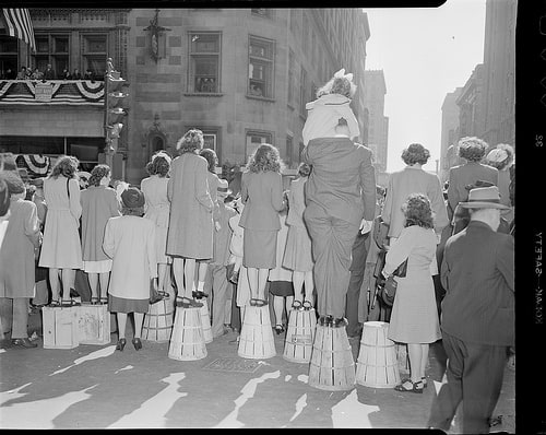 People standing on baskets to watch a procession. 