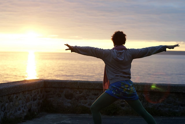 Woman doing yoga in front of the sunrise over the ocean. 
