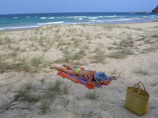 Woman sunning on the beach with a basket.