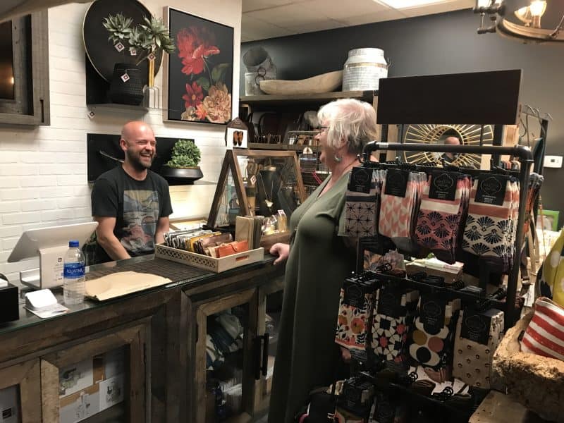 A shopkeeper and a customer share a laugh in a small store packed full of interesting home wares. 