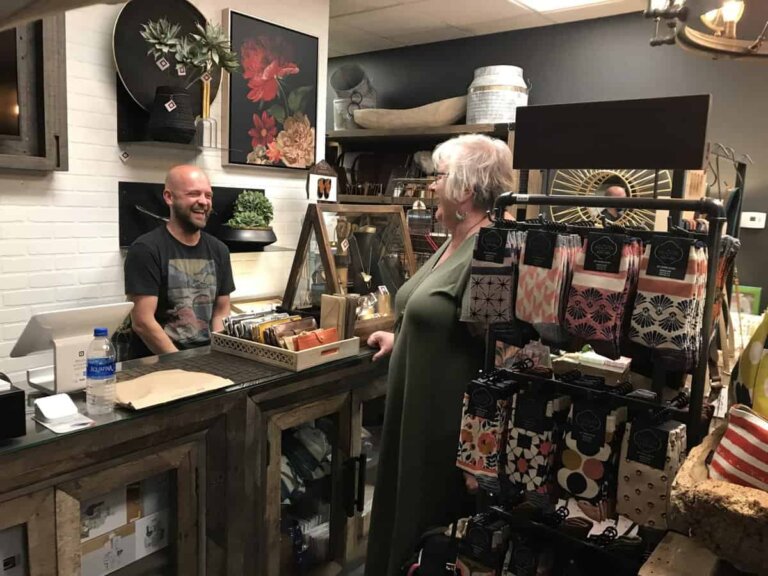 A shopkeeper and a customer share a laugh in a small store packed full of interesting home wares.
