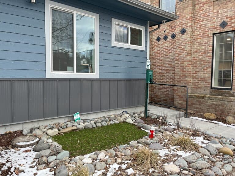 In front of a downtown building, a small rectangle of turf grass provides a pet relief area. A bag dispenser is mounted on a pole nearby.