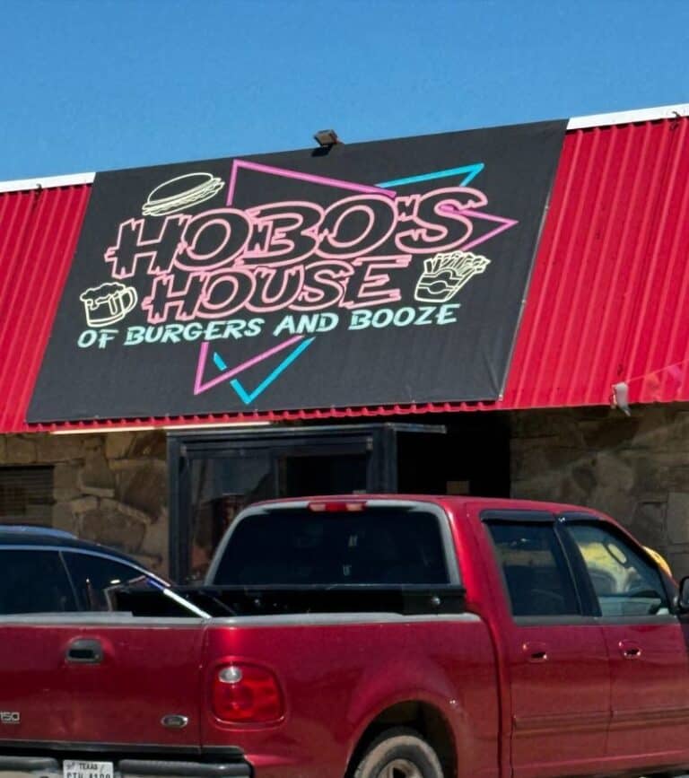The front of a restaurant features a neon style sign that says "Hobo's House of Burgers and Booze."