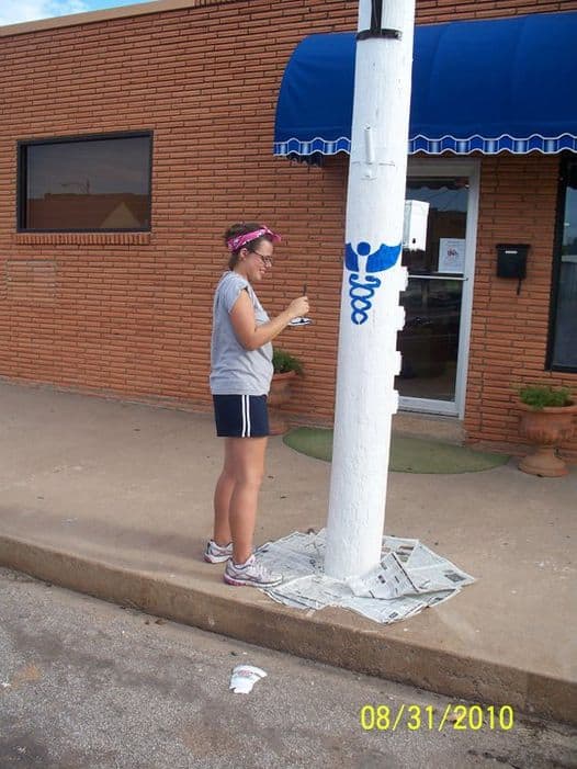 Woman painting a utility pole with a medical symbol in front of a medical office