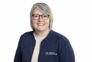 A woman wearing glasses with short hair of mixed silver and blonde, wearing a jacket that says Dakota Resources